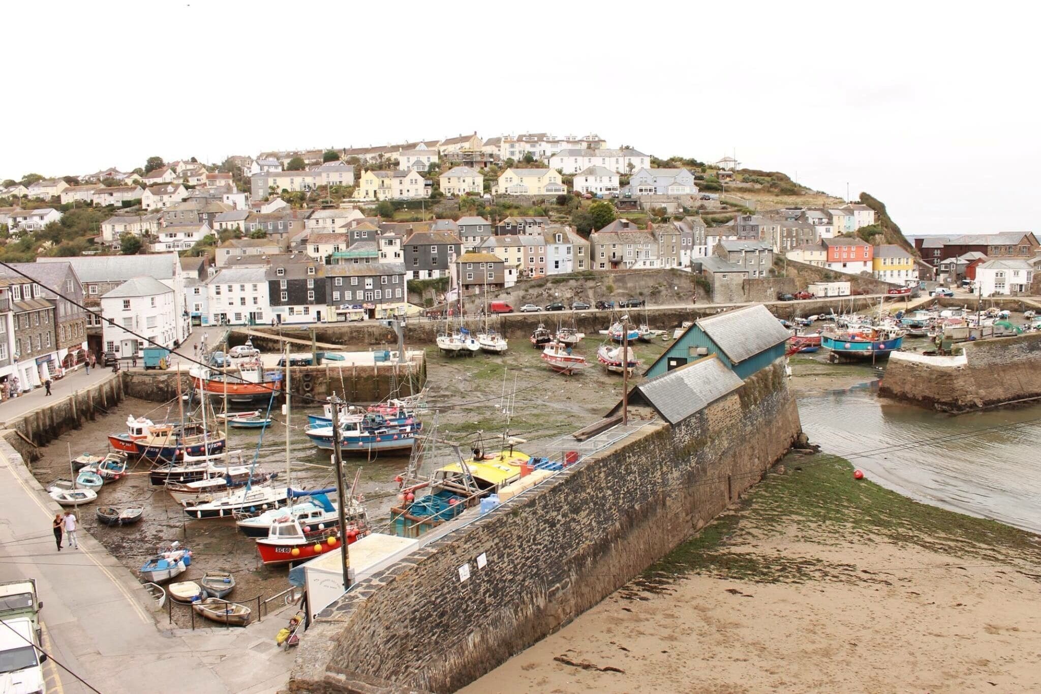 A harbor with boats, a stone wall, and houses on a hillside.
