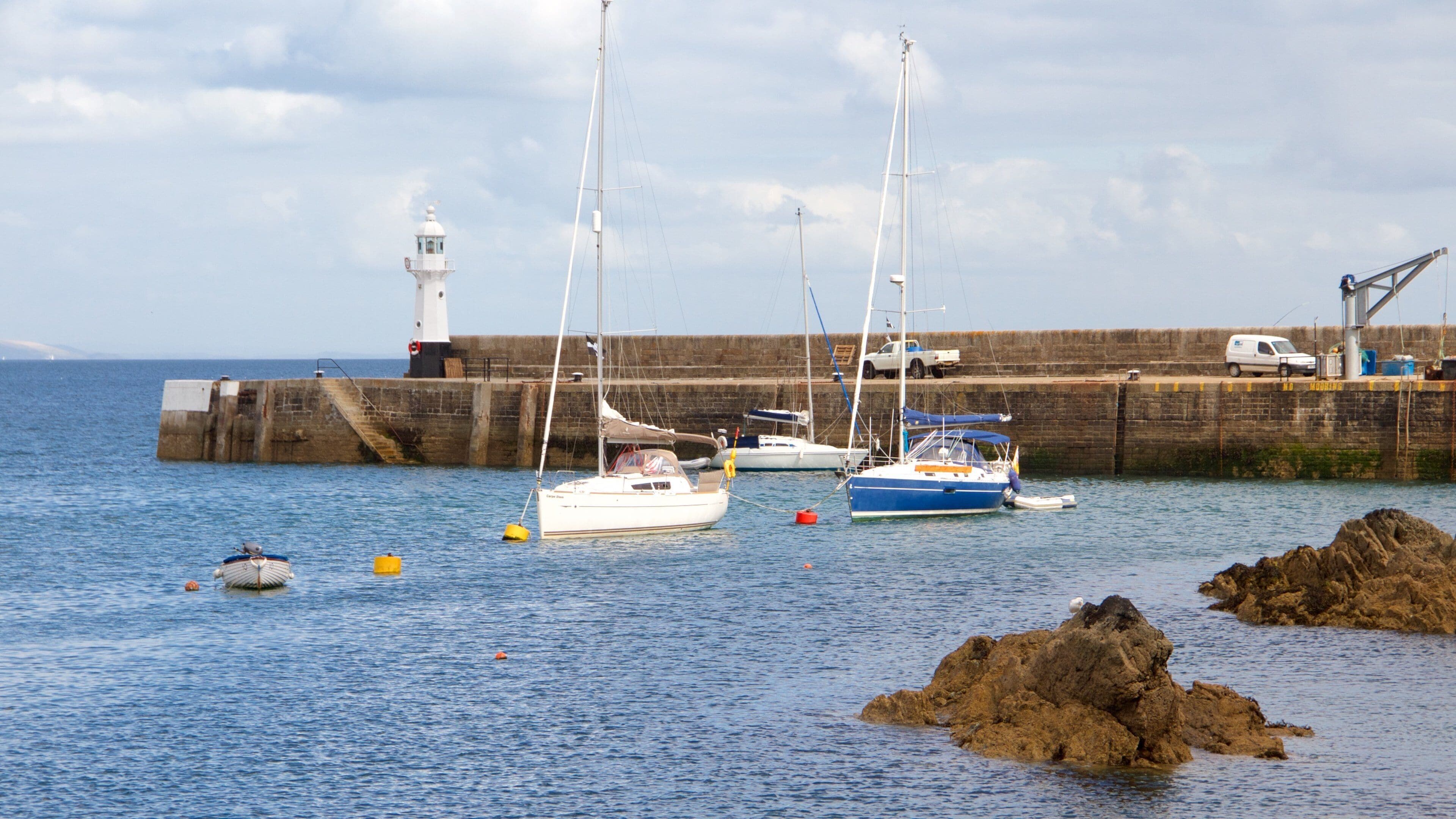 A harbor with boats, a lighthouse, and a rocky outcrop.