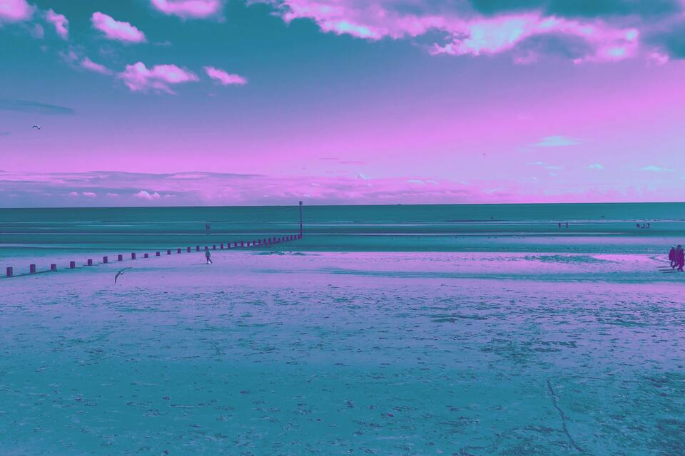 A beach with a wooden jetty and people walking along the shore.