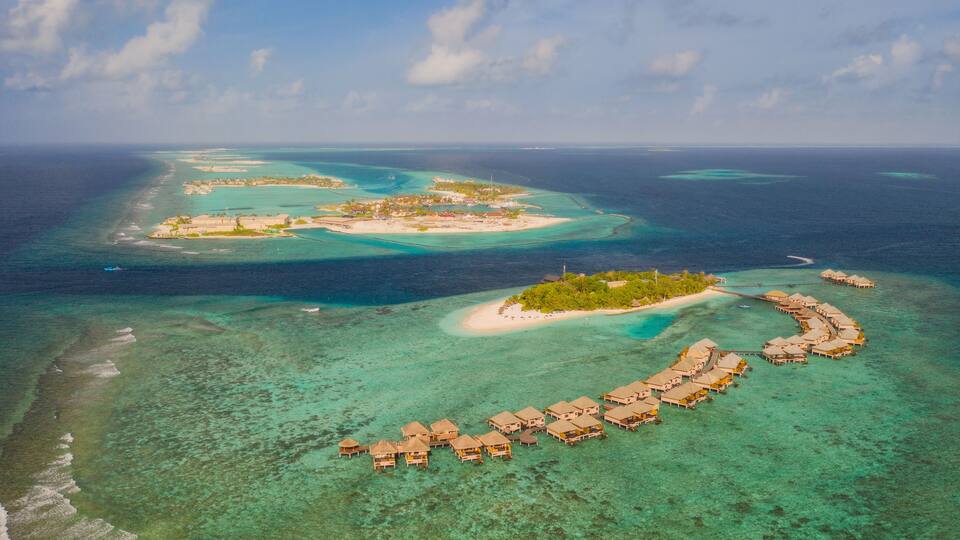 An aerial view of a tropical island with clear turquoise waters, a crescent-shaped resort, and several smaller islands in the background.