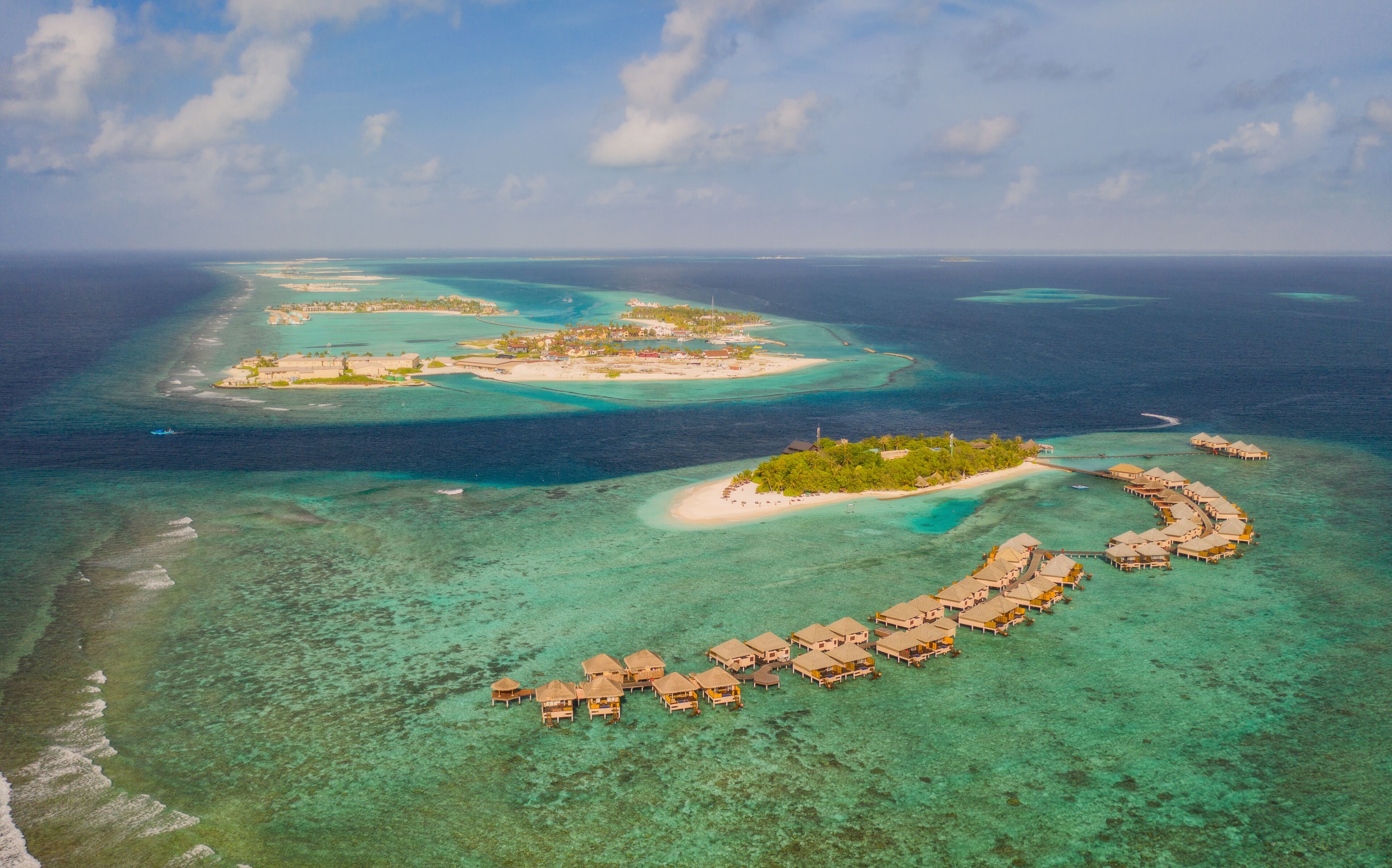 An aerial view of a tropical island with clear turquoise waters, a crescent-shaped resort, and several smaller islands in the background.