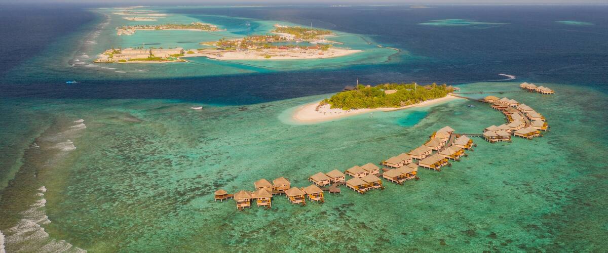 An aerial view of a tropical island with clear turquoise waters, a crescent-shaped resort, and several smaller islands in the background.