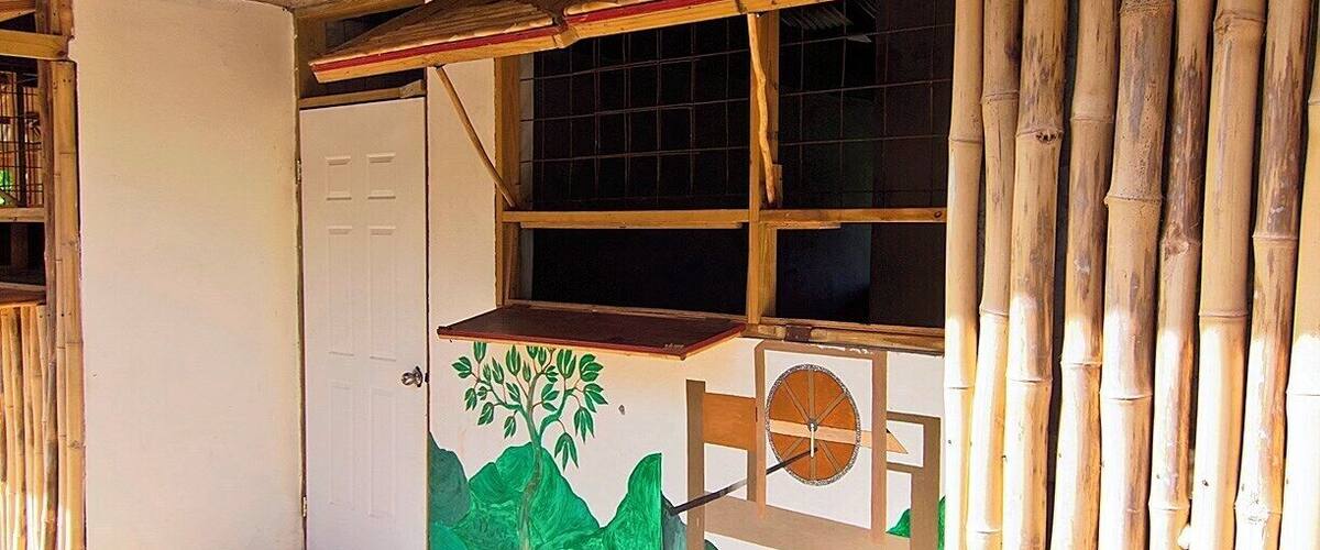 A room with a white door, a window with a grid pattern, and a mural of green mountains and a tree.