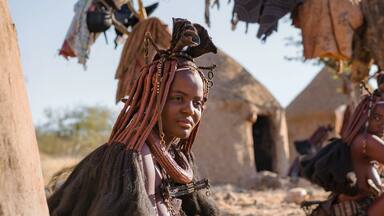 Panoramic shot showing Himba tribeswomen sitting outside their huts in a traditional Himba village near Kamanjab in northern Namibia, Africa.