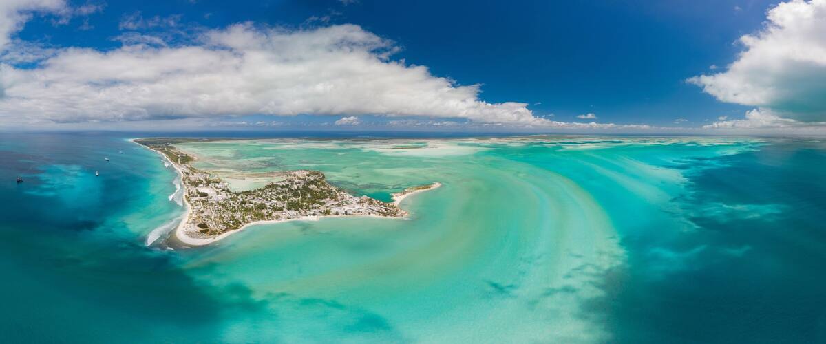 An aerial view of a turquoise island with clear waters and a sandy beach.