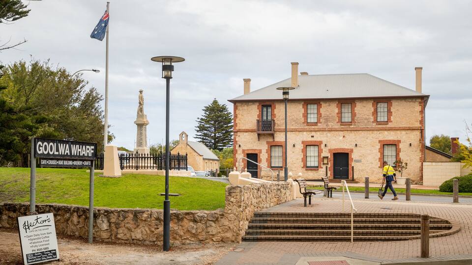 A historic building with a stone facade, a flagpole with the Australian flag, and a sign for 'Goolwa Wharf' with amenities listed.