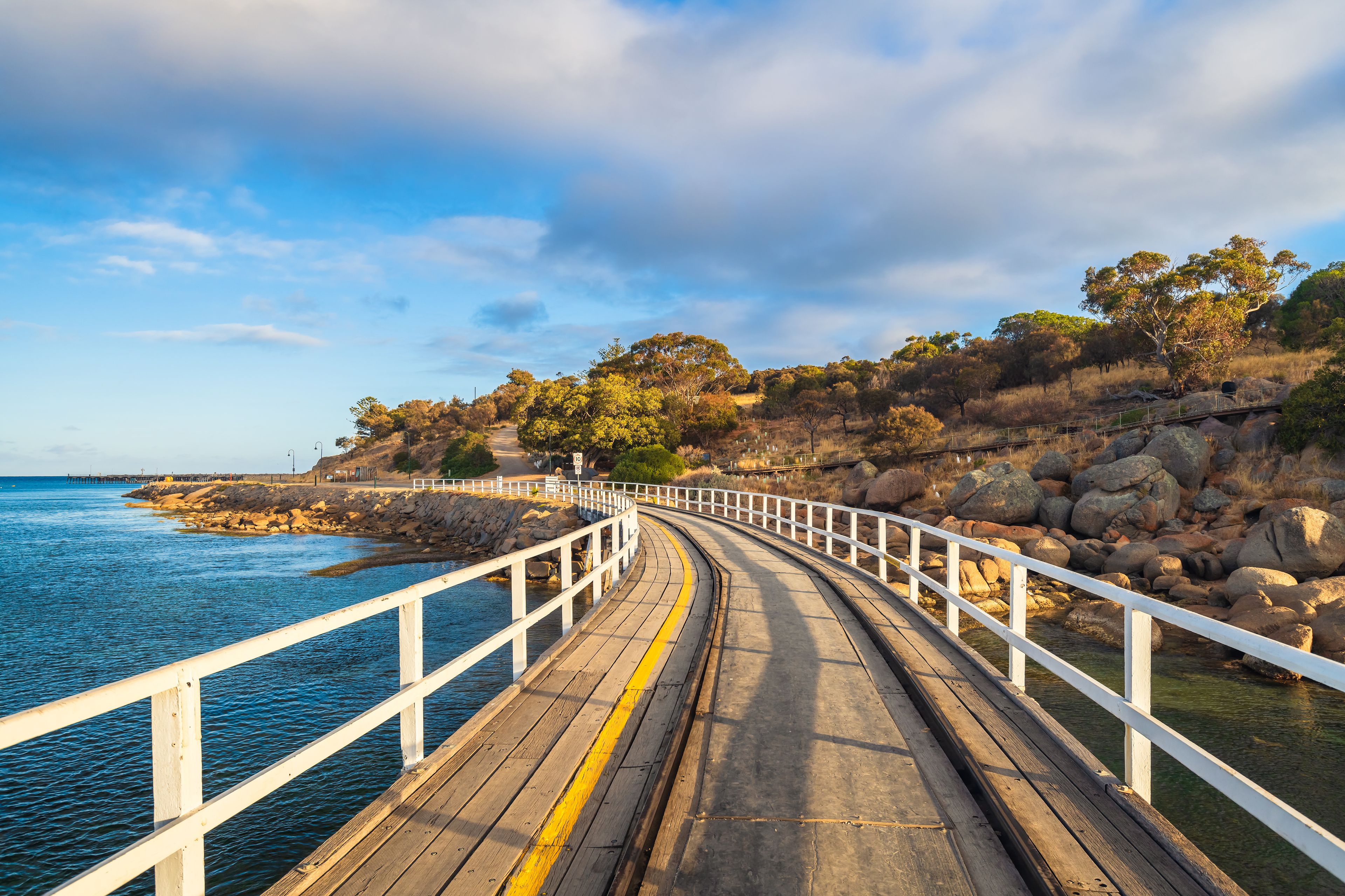 A wooden boardwalk leading to a rocky shoreline with a clear blue sky above.
