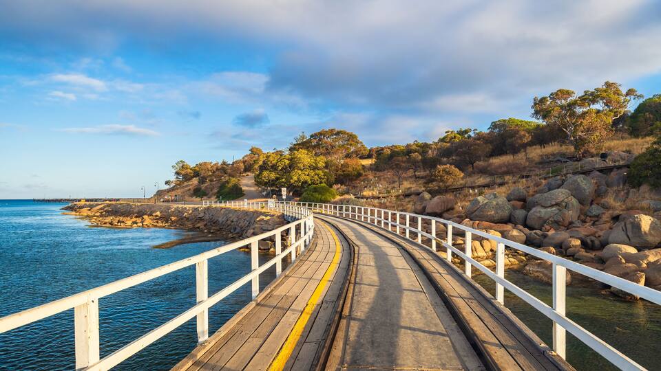 A wooden boardwalk leading to a rocky shoreline with a clear blue sky above.