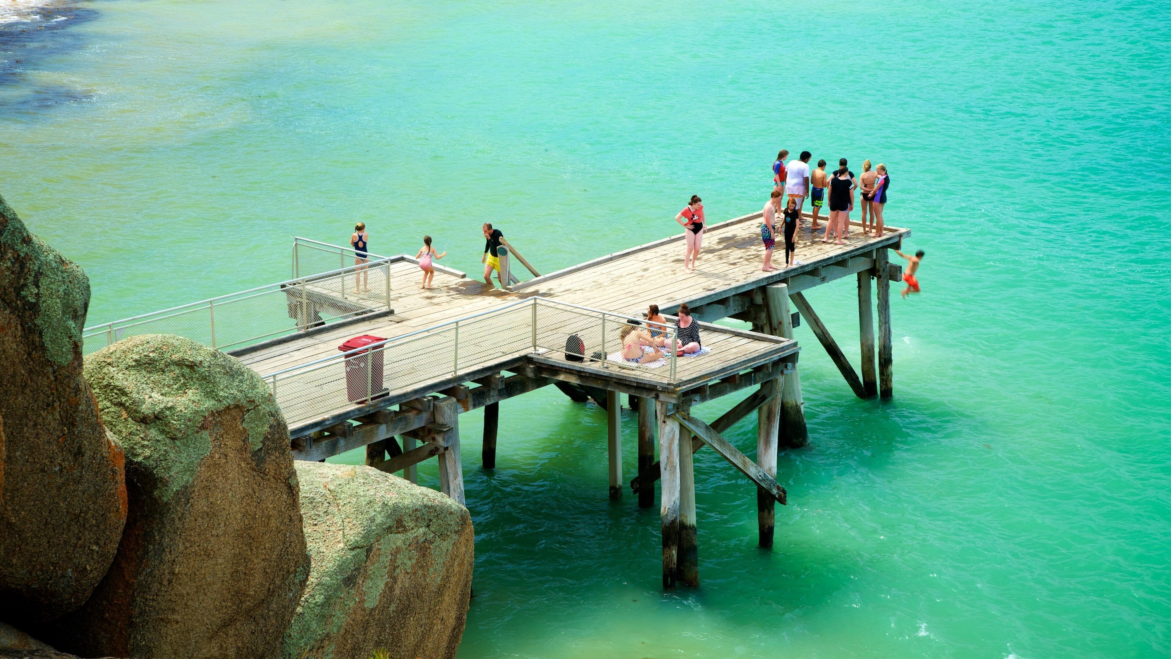 A pier extending into turquoise water with people walking and standing on it.