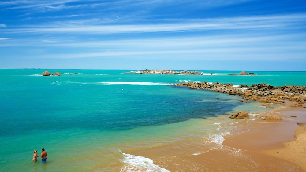 A beach with clear turquoise water, rocky outcrops, and a distant island.