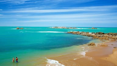 Una playa con agua turquesa cristalina, afloramientos rocosos y una isla distante.