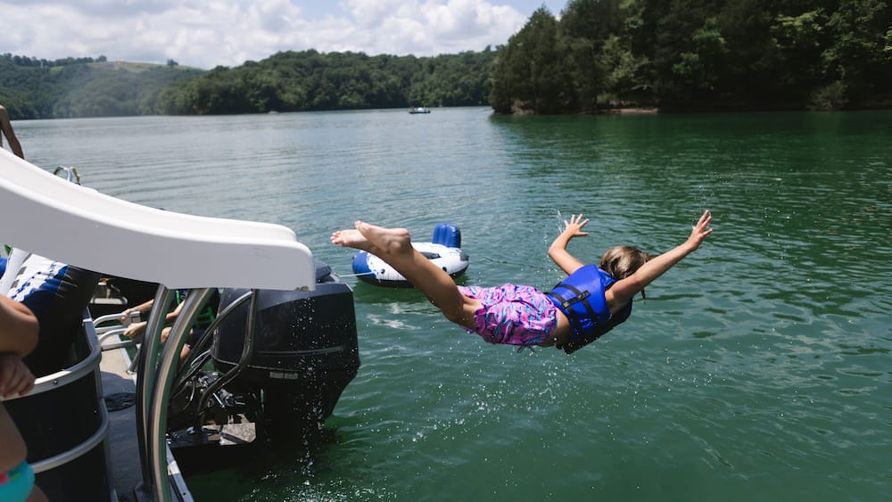 Child sliding off pontoon boat slide into lake on belly