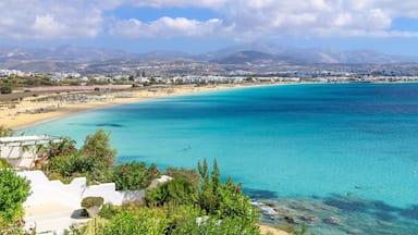 A coastal landscape with clear turquoise waters, a sandy beach, and a backdrop of mountains.