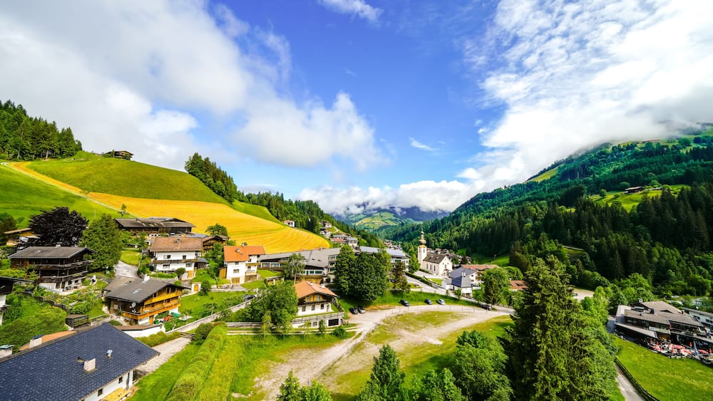 A village nestled in a valley with houses, a church, and a mountain backdrop.