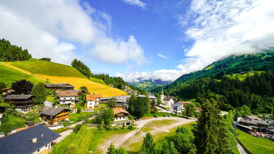 A village nestled in a valley with houses, a church, and a mountain backdrop.