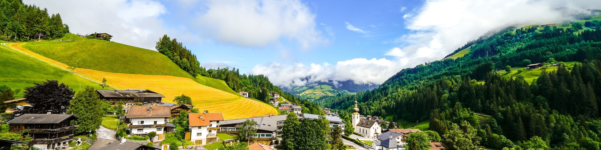 A village nestled in a valley with houses, a church, and a mountain backdrop.