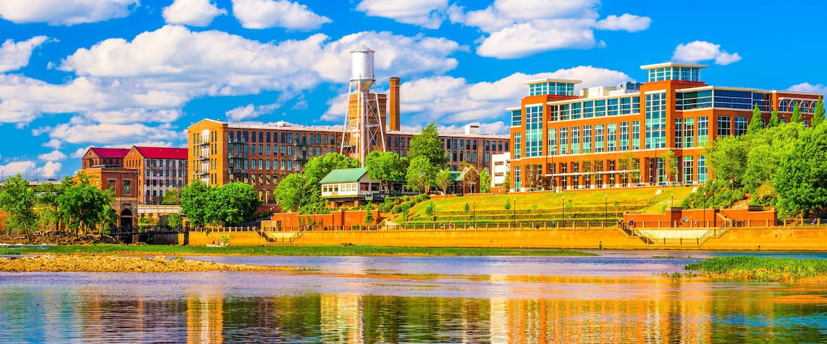A riverside cityscape with modern buildings, a water tower, and lush greenery.