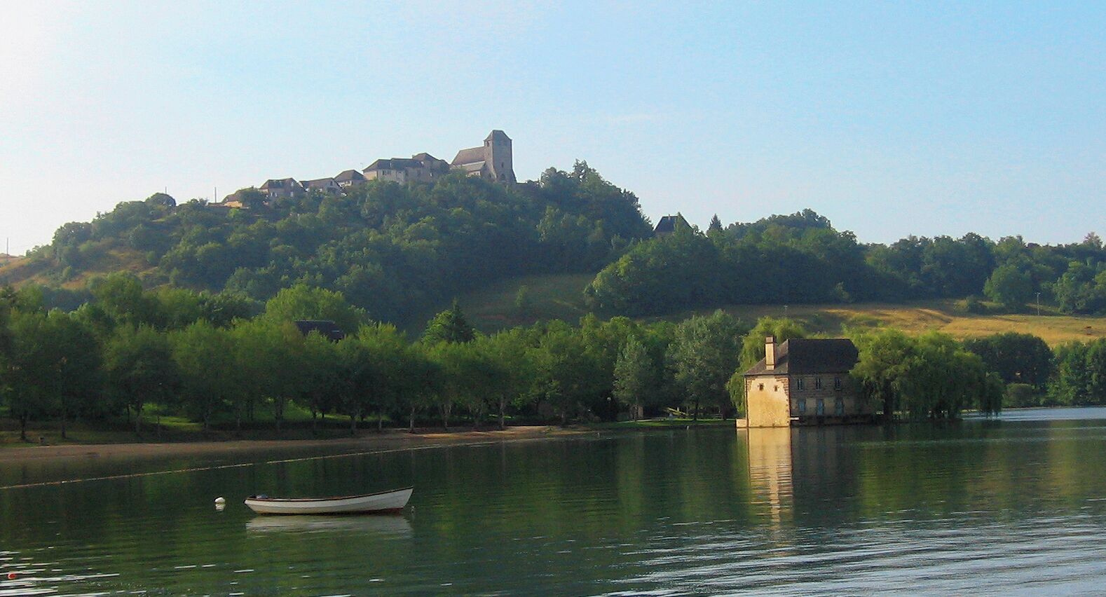 A calm lake with a small boat, a church on a hill, and a house on the shore.