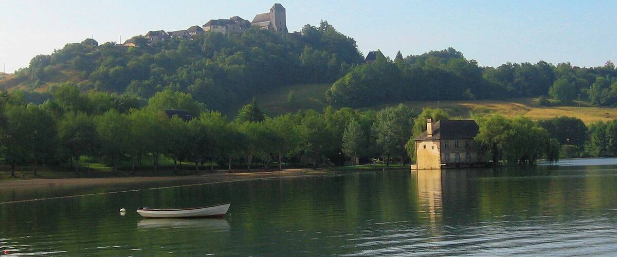 A calm lake with a small boat, a church on a hill, and a house on the shore.