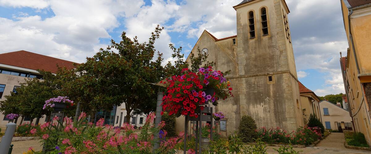 A church with a tall bell tower, surrounded by colorful flowers and trees.