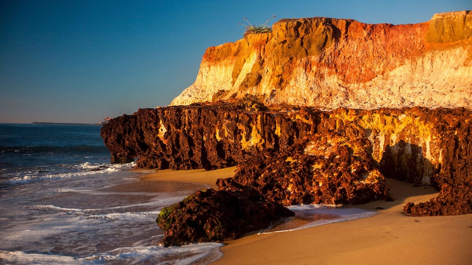 A coastal landscape with a rocky cliff, sandy beach, and ocean waves.