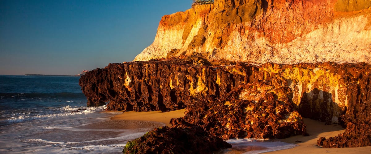 A coastal landscape with a rocky cliff, sandy beach, and ocean waves.