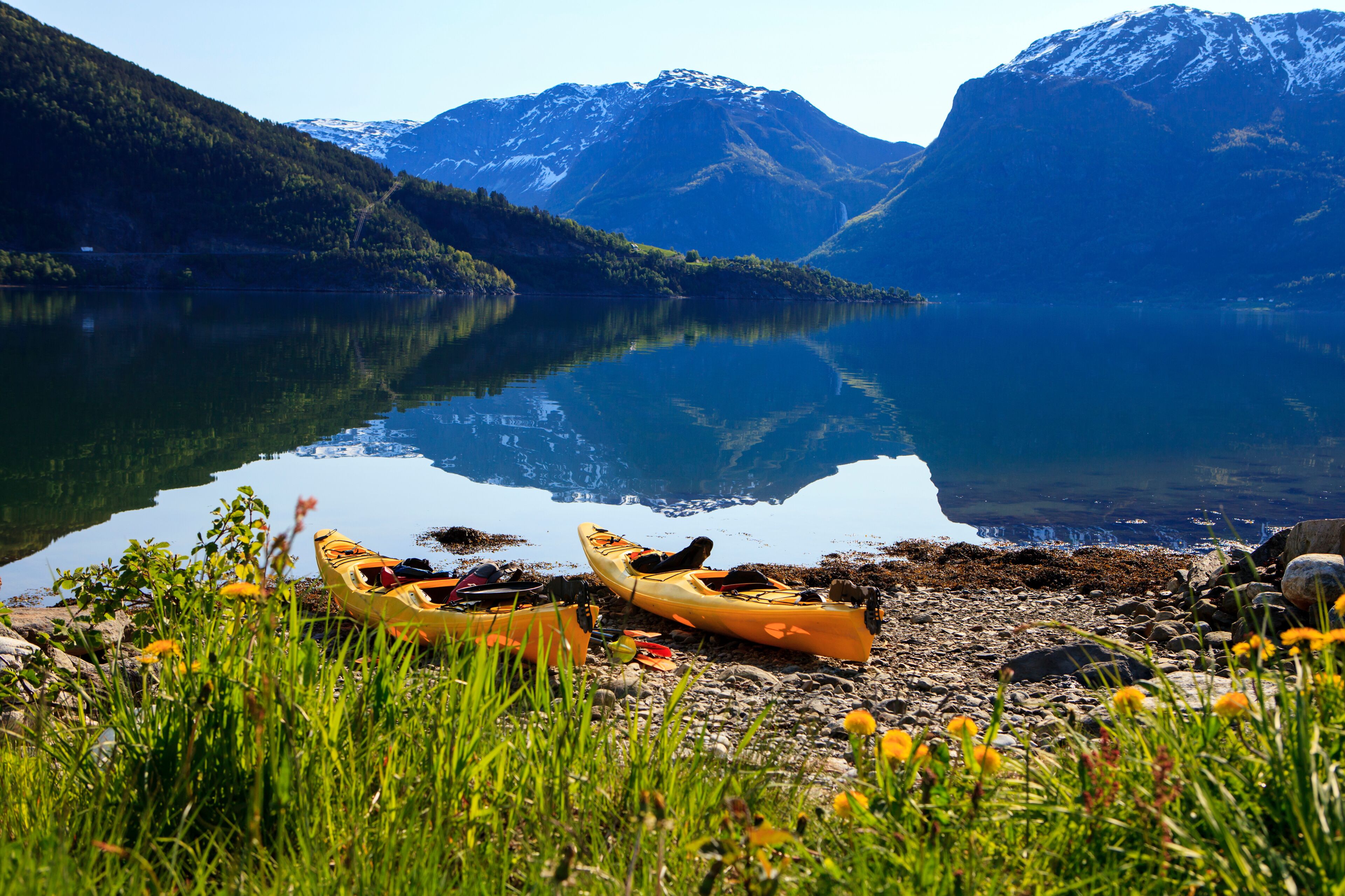 A calm lake with kayaks on the shore, surrounded by mountains and greenery.