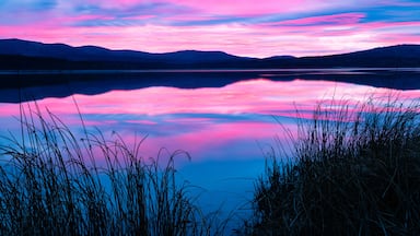Un lago tranquilo con el reflejo del cielo, rodeado de hierba y montañas.