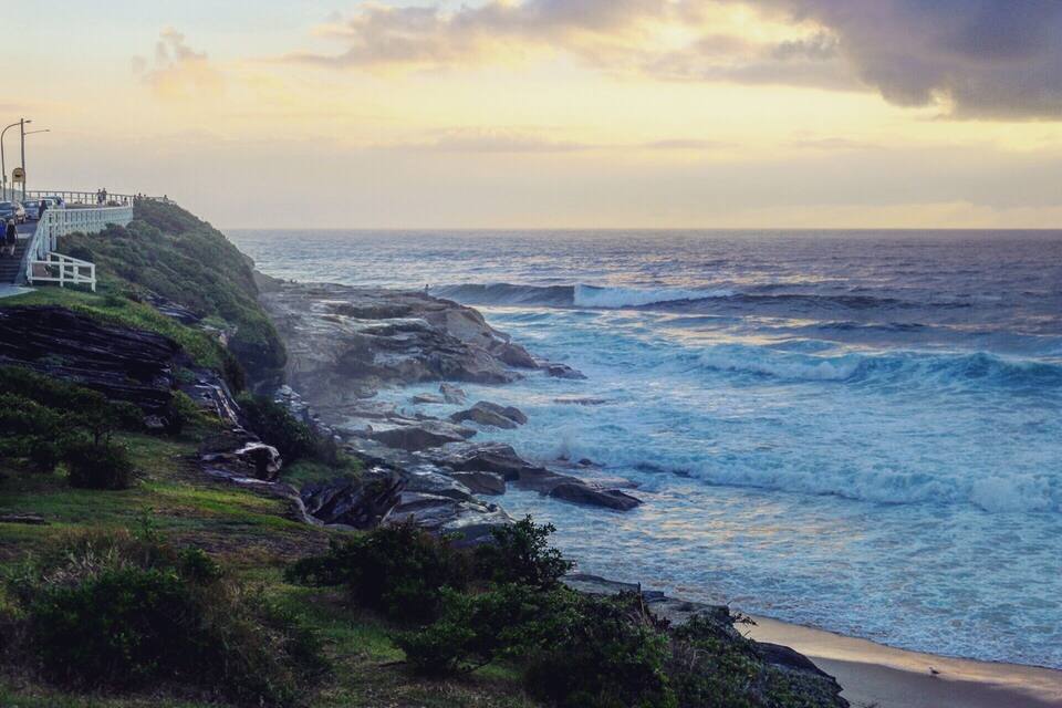 A coastal landscape with rocky cliffs, a sandy beach, and a staircase leading down to the shore.