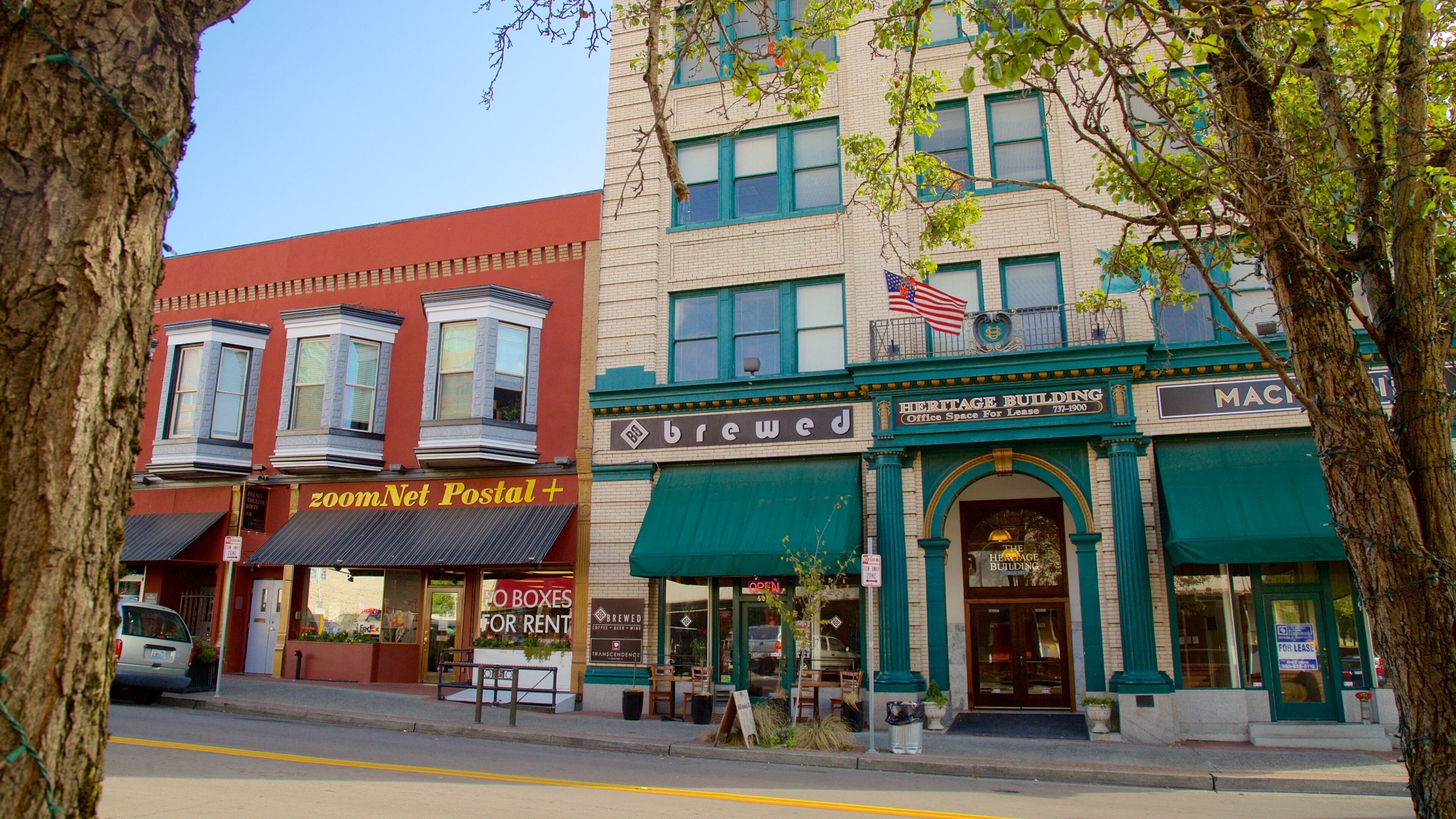 A street with buildings, including a red building with a 'zoomNet Postal' sign and a green building with a 'Heritage Building' sign.