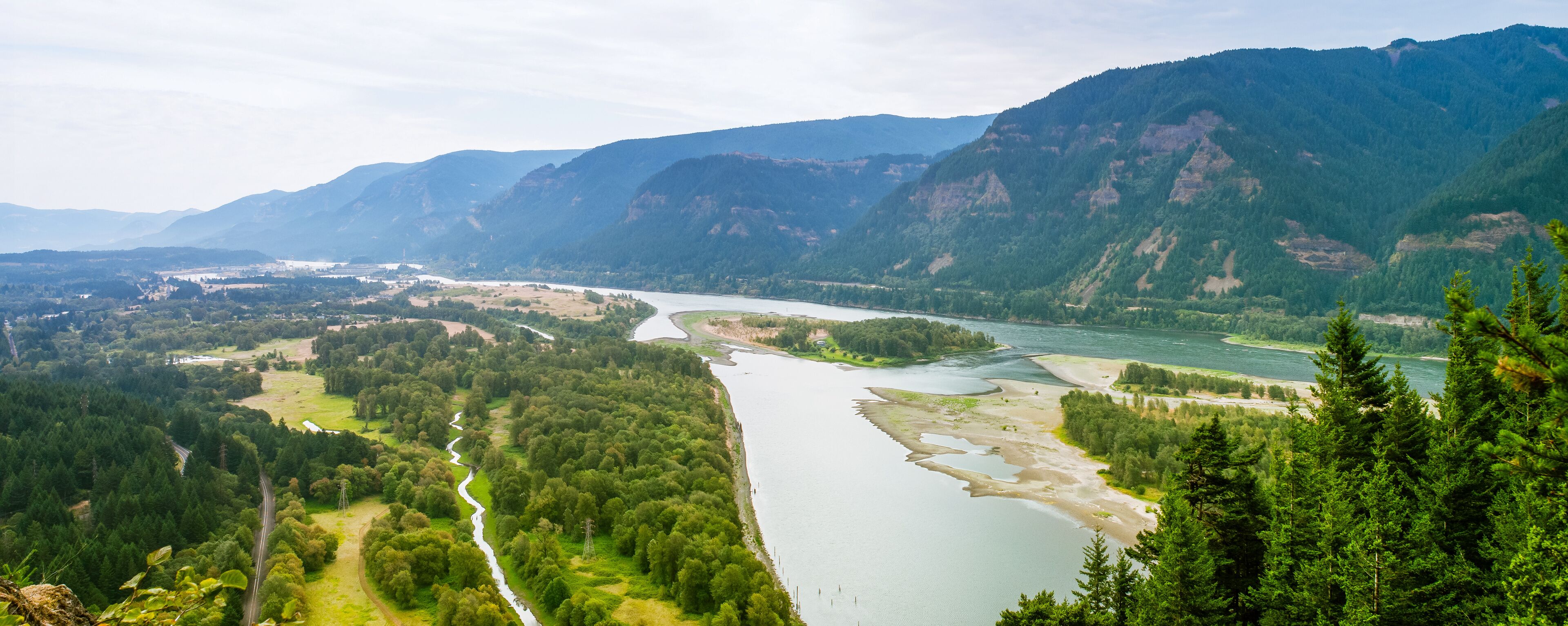 A river winding through a valley with dense forests and mountains in the background.
