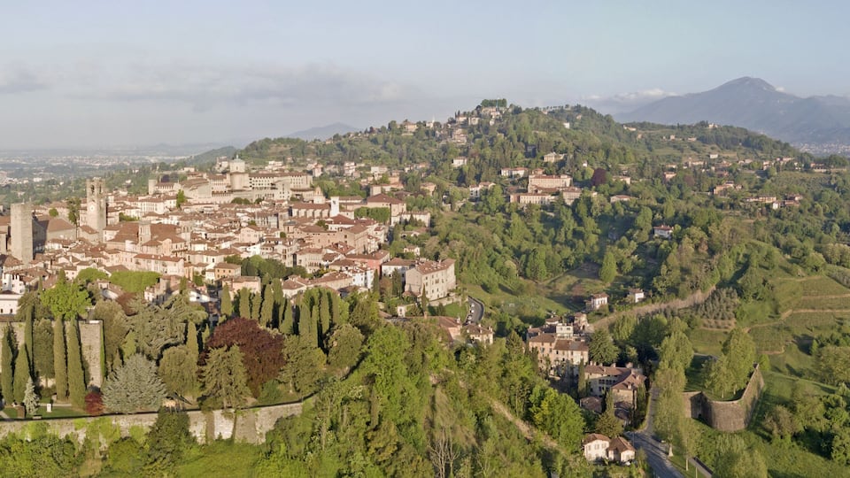 A historic town with medieval architecture, surrounded by lush greenery and hills.