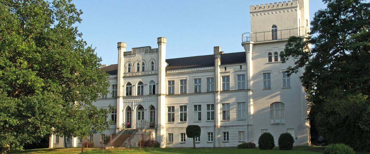 A large, historic building with multiple towers and a well-maintained lawn.
