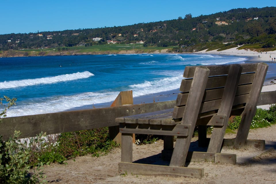 A wooden chair overlooking a beach with waves crashing onto the shore.