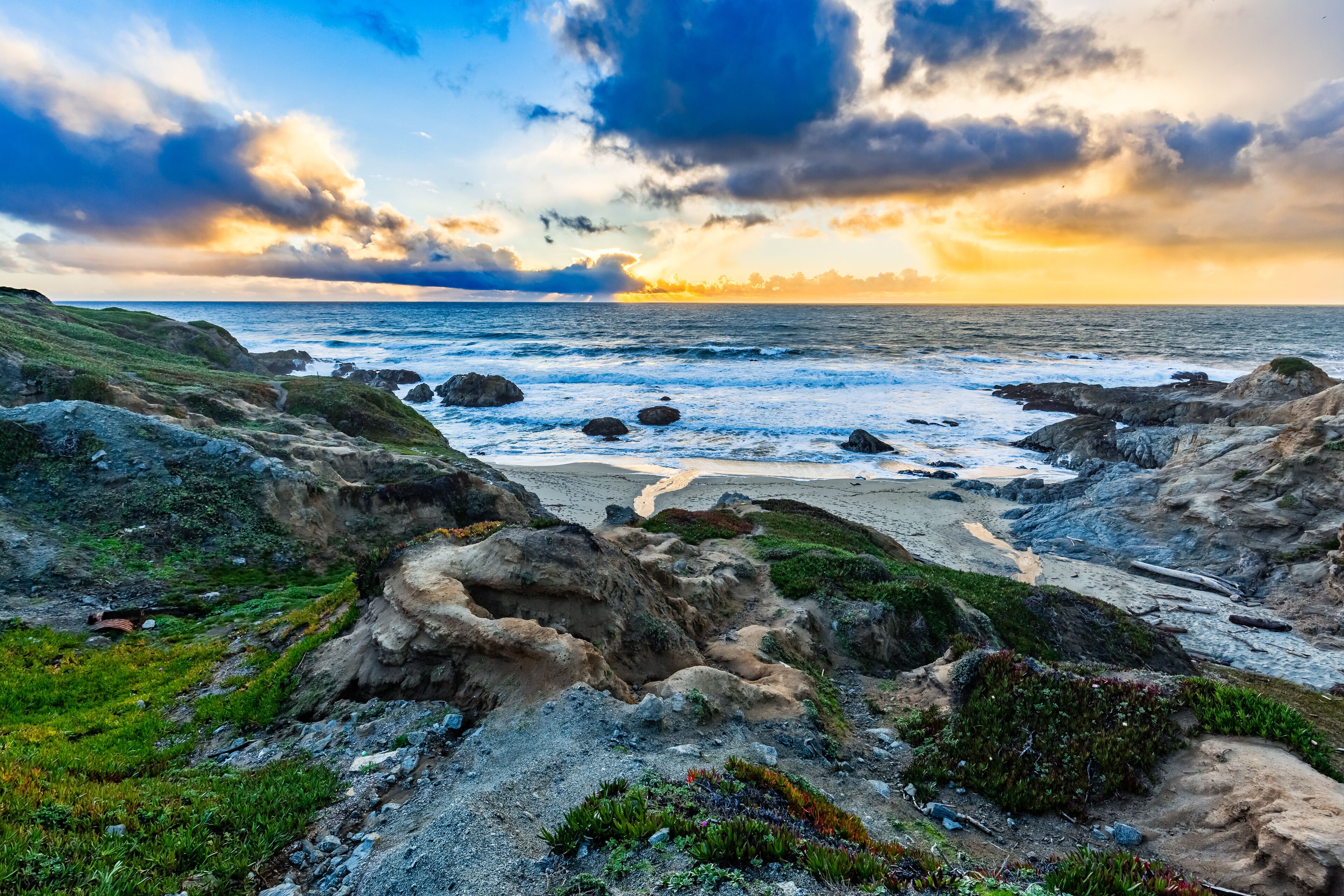 A rocky coastline with waves crashing against the shore under a dramatic sunset sky.
