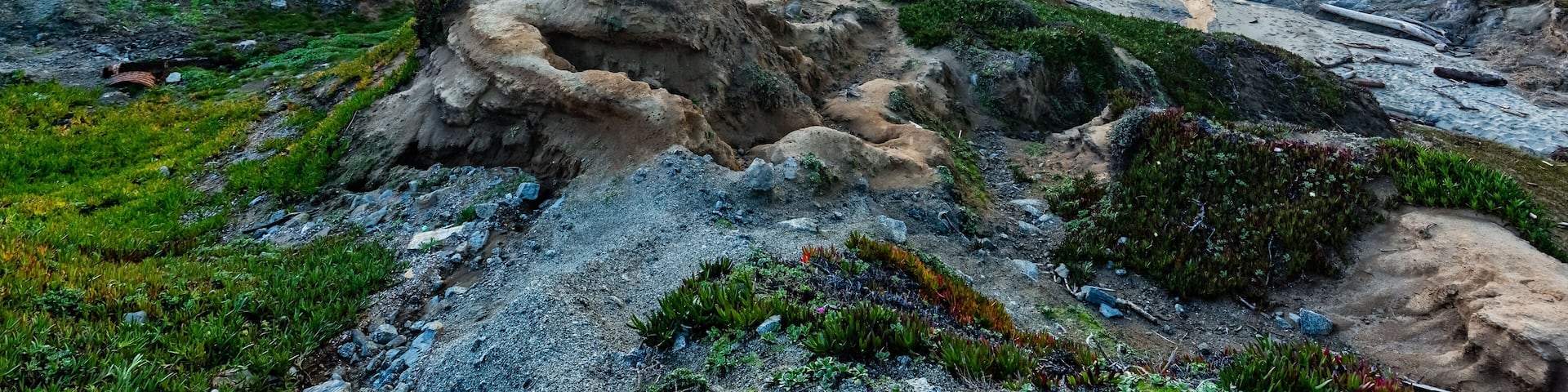 A rocky coastline with waves crashing against the shore under a dramatic sunset sky.