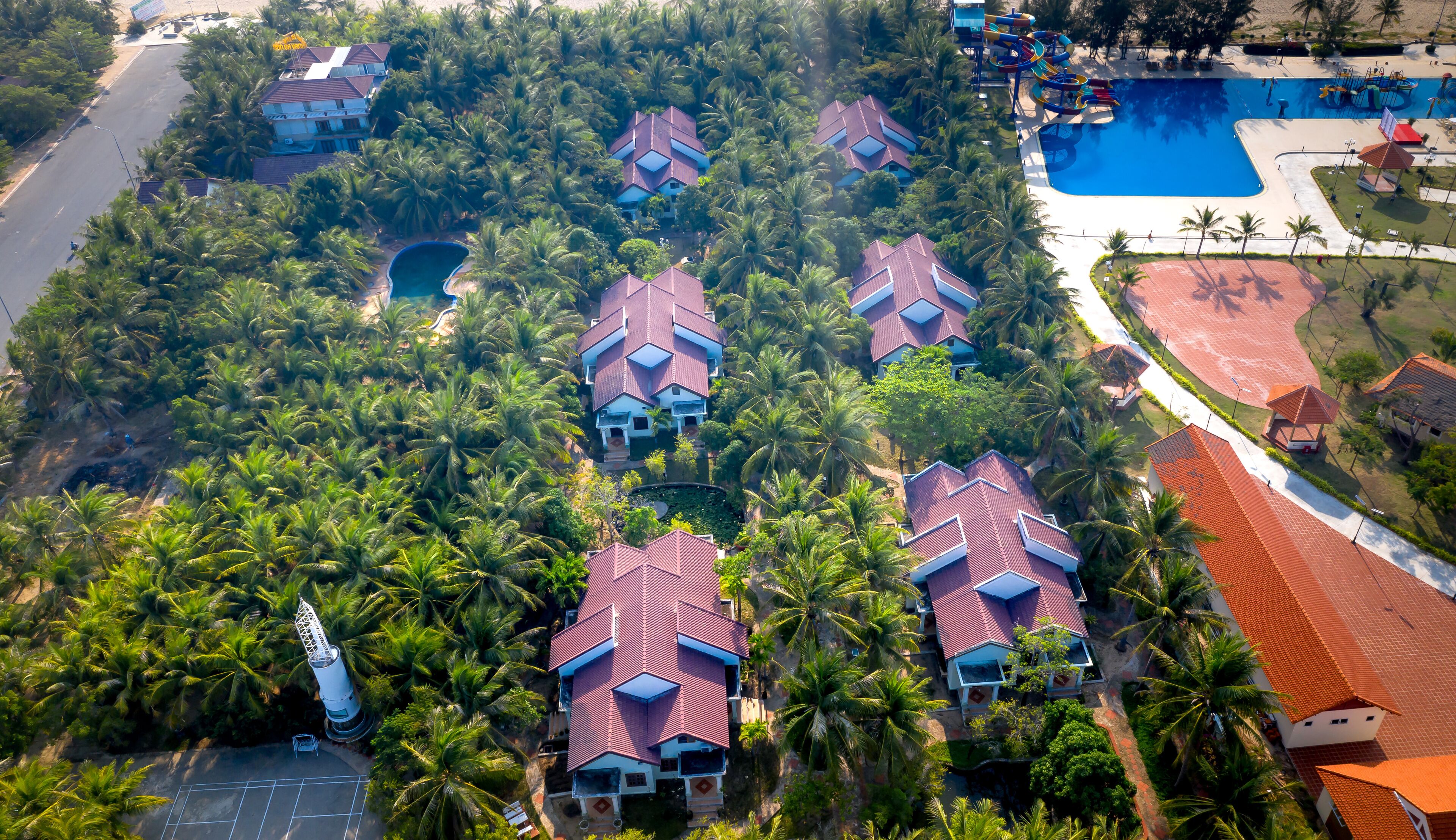 An aerial view of a residential area with multiple houses, palm trees, and a swimming pool.