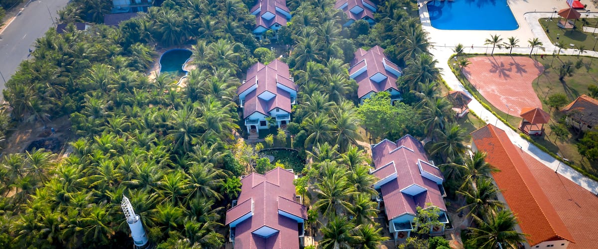 An aerial view of a residential area with multiple houses, palm trees, and a swimming pool.