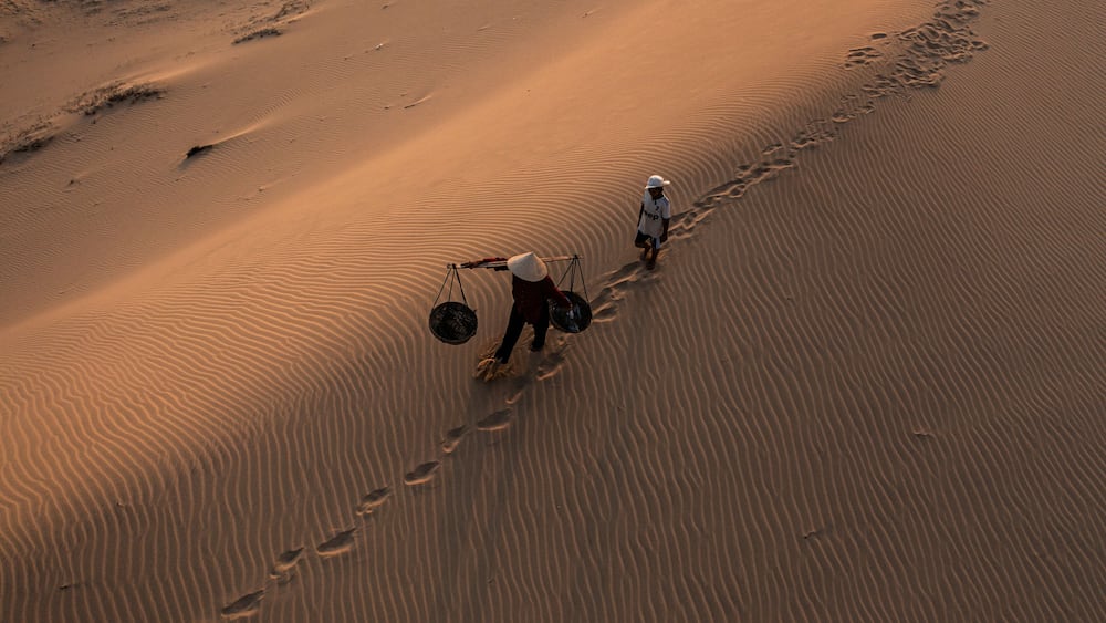Un vaste paysage dĂ©sertique, avec des dunes de sable ondulĂ©es, et deux personnes qui marchent le long dâun sentier.