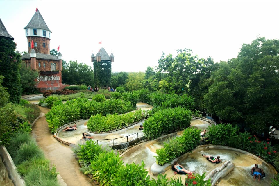 A castle with towers, a winding water channel, and lush greenery.