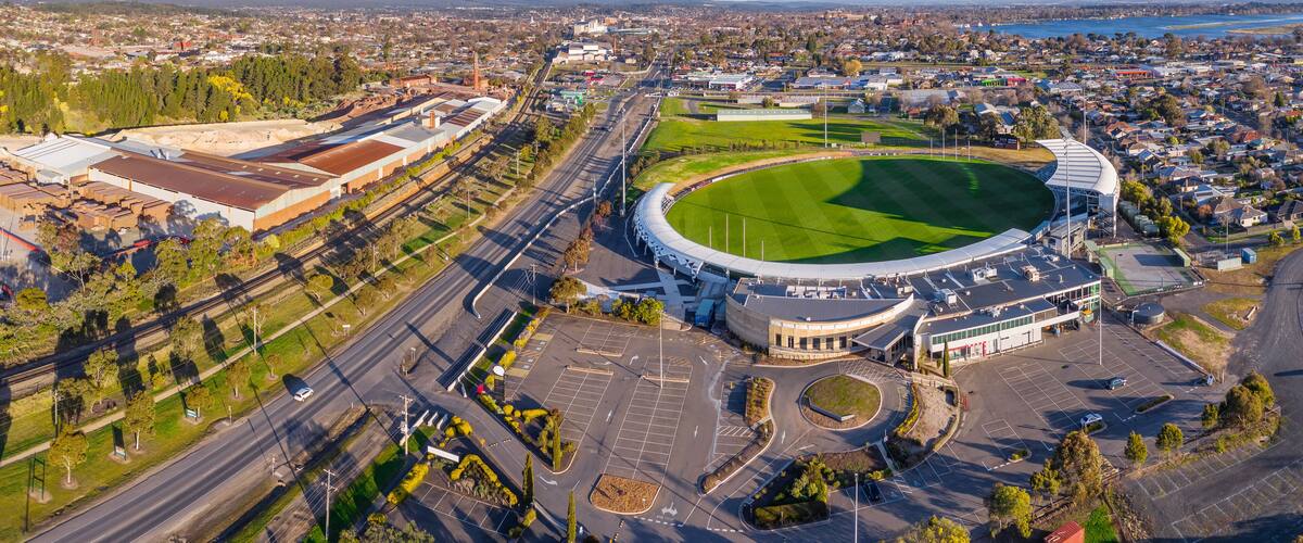 Aerial panorama of a city arterial road separating a factory and a football oval and carpark