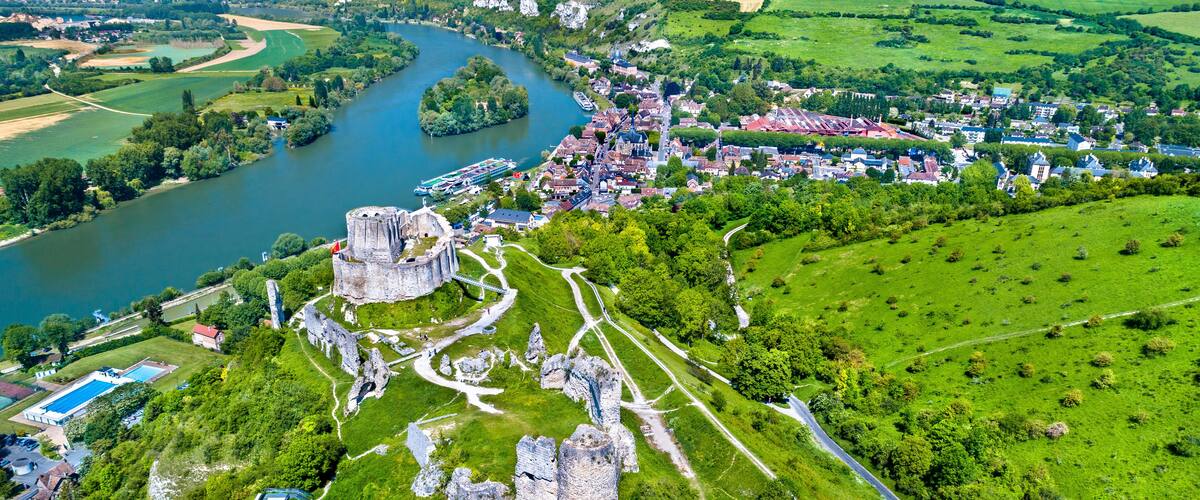 A historic castle surrounded by lush greenery, a river, and a small town.