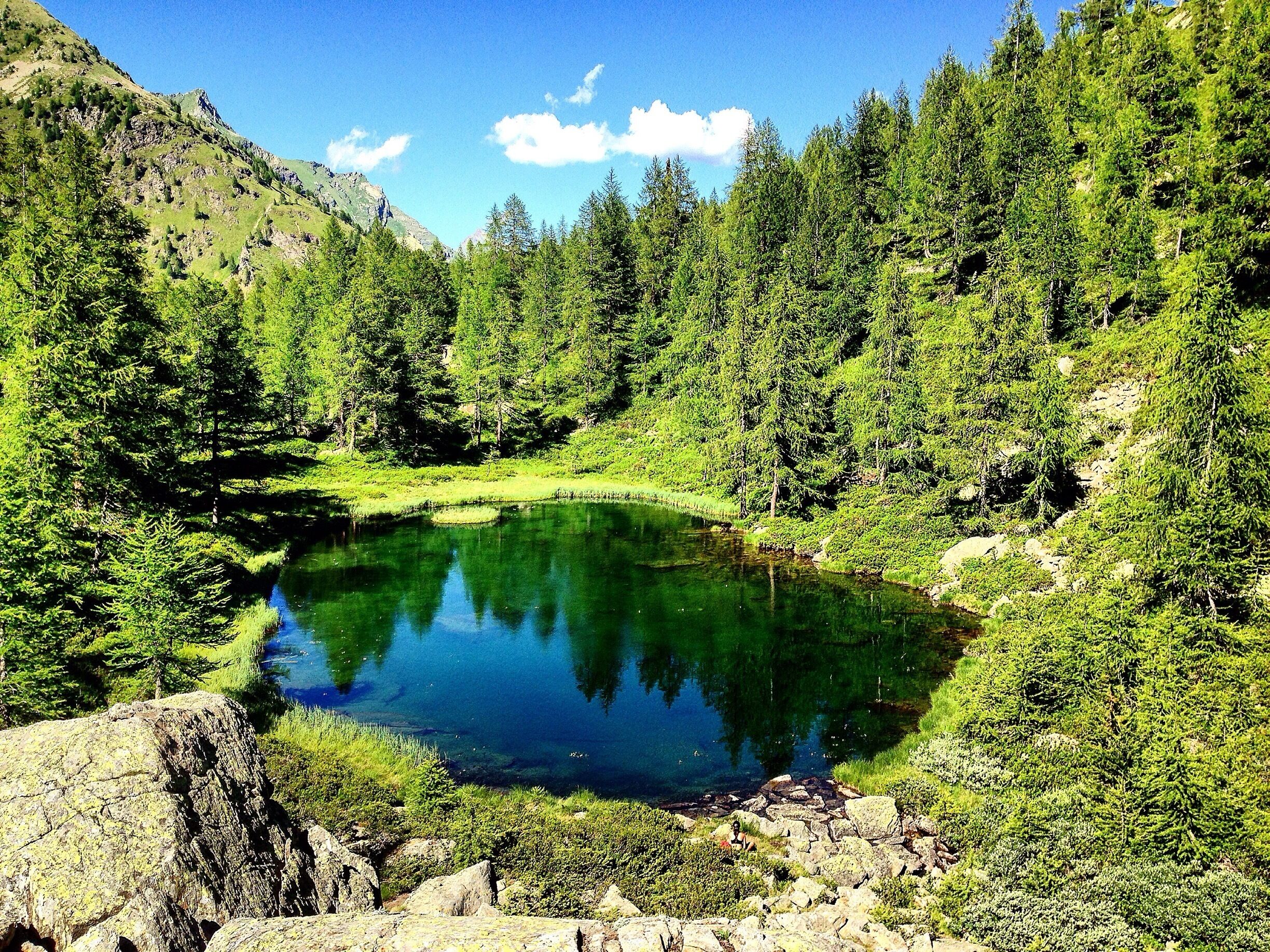 A clear mountain lake surrounded by dense forest and rocky terrain.