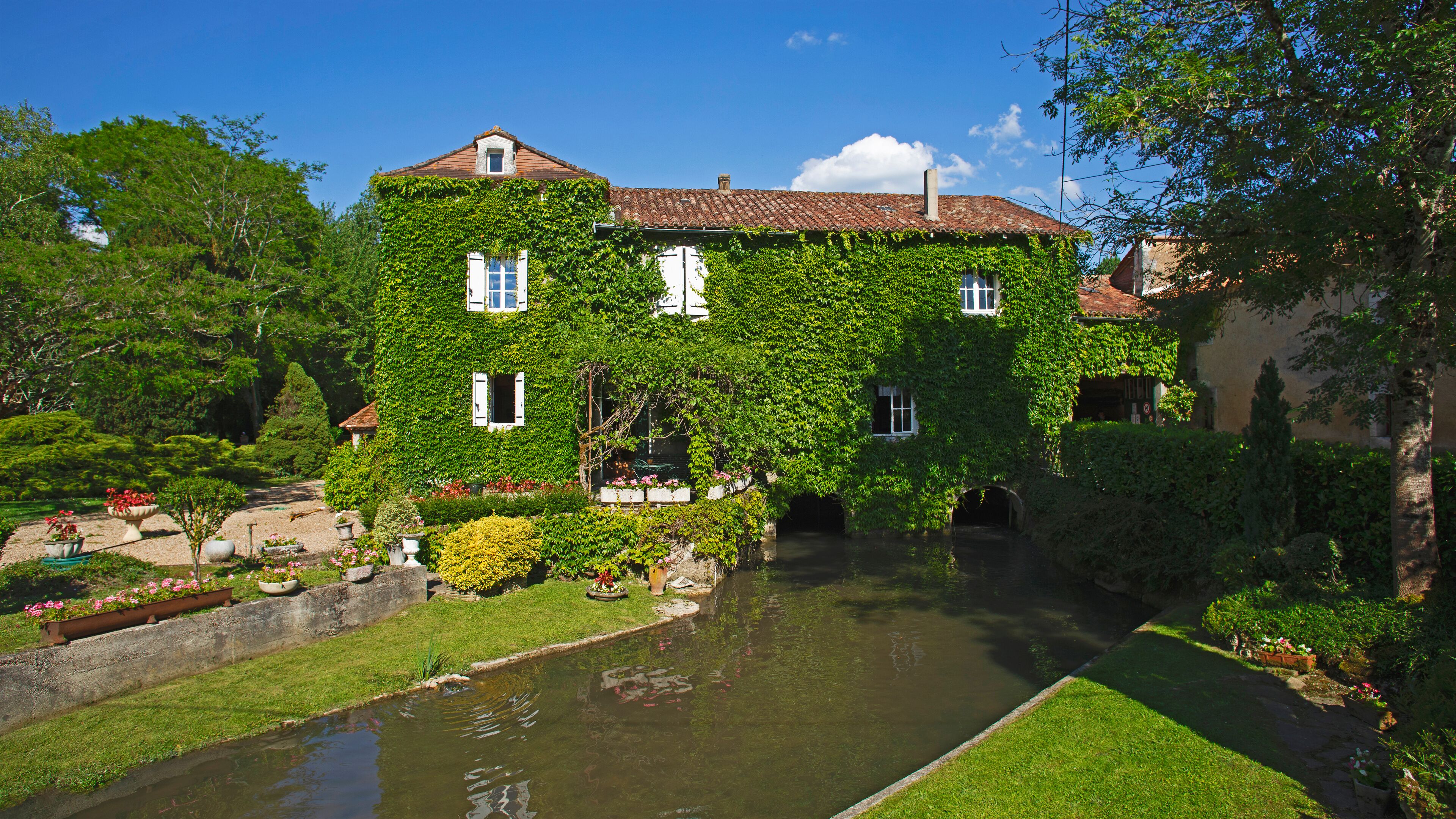 A house covered in green ivy, a canal, and lush gardens.