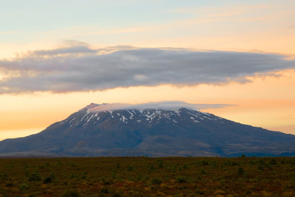 A snow-capped mountain with a clear sky and a flat landscape in the foreground.