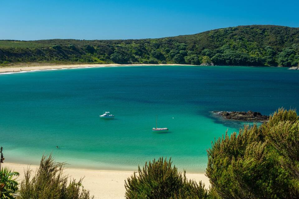 A coastal landscape with a sandy beach, turquoise waters, and a boat anchored near the shore.