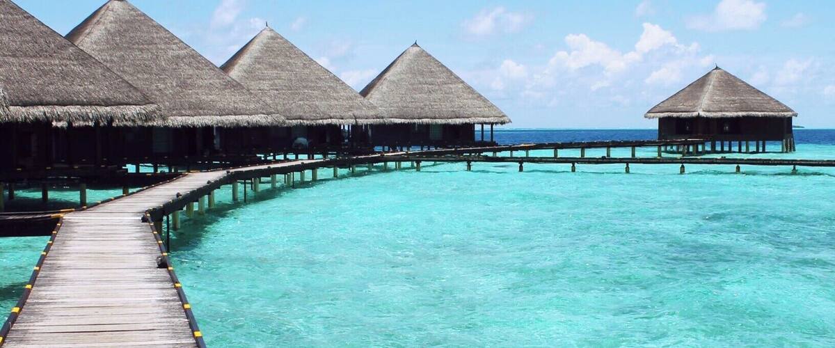 A wooden pier leading to overwater bungalows with thatched roofs.