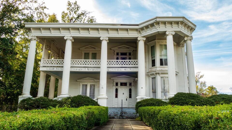A white colonial-style house with a porch, columns, and a well-maintained garden.
