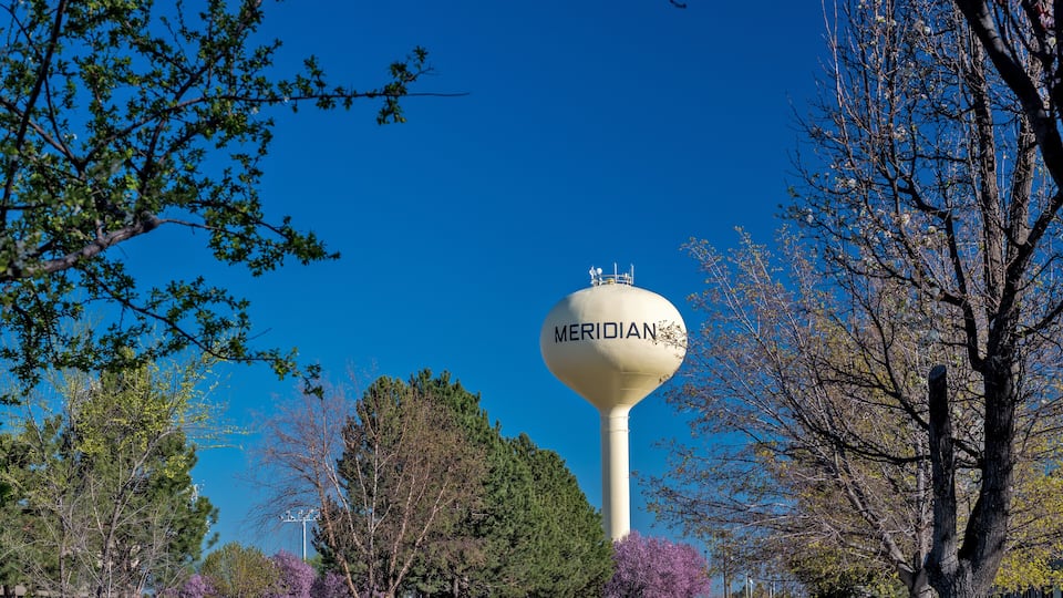 A water tower labeled 'MERIDIAN' surrounded by trees and a clear blue sky.