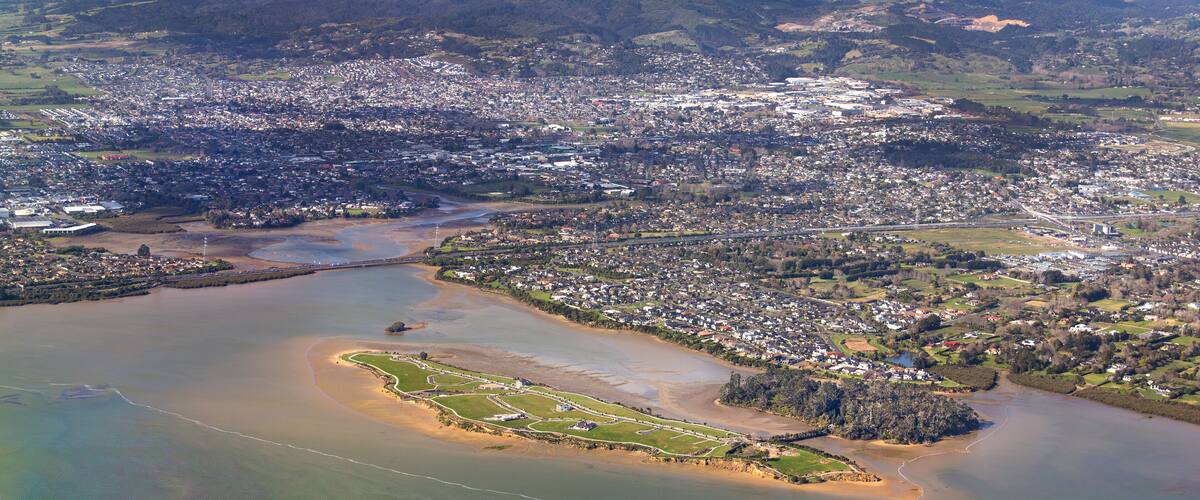 An aerial view of a coastal city with a river, a beach, and surrounding greenery.